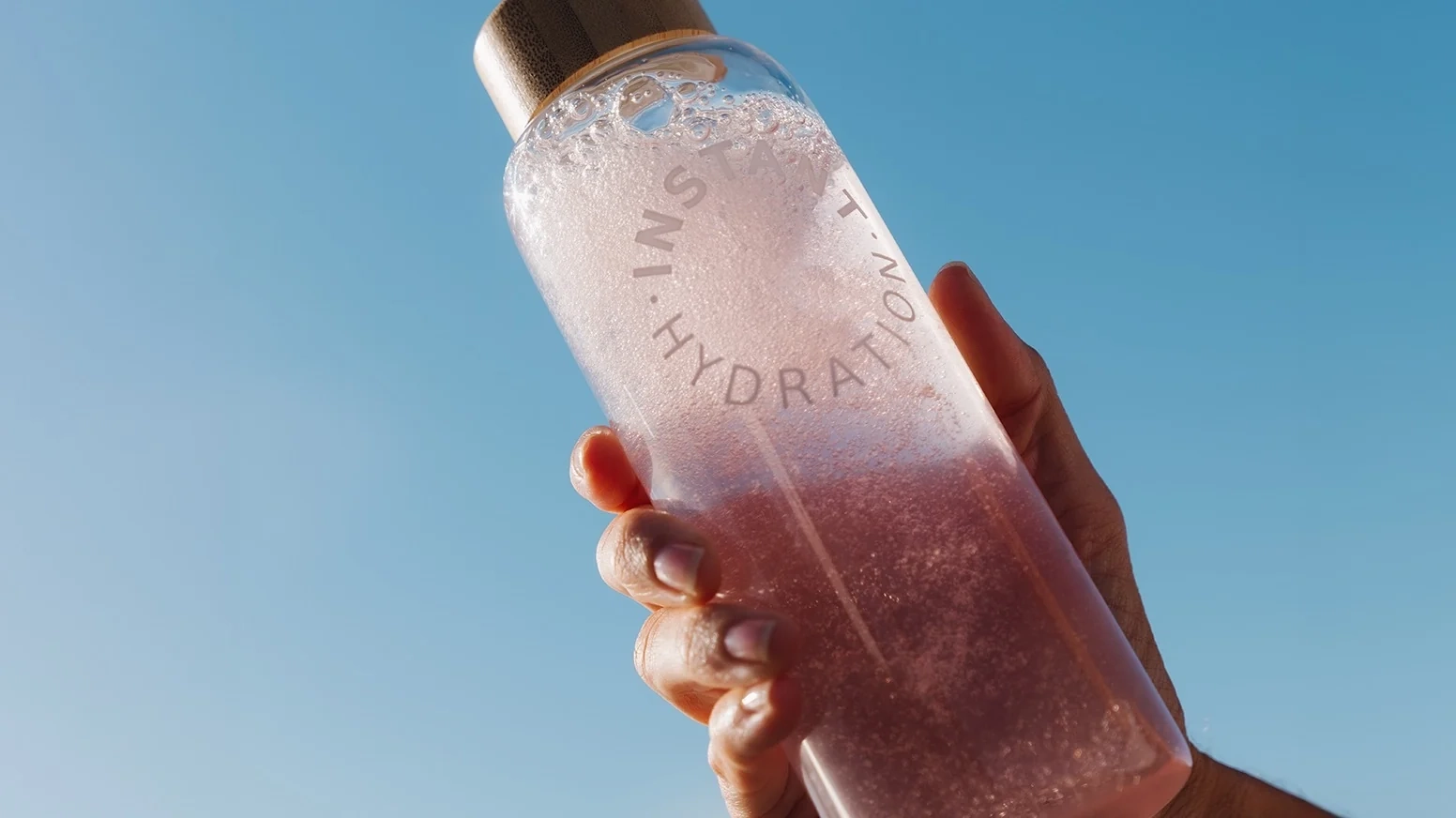 Person holding a pink bottle labeled 'Instant Hydration' with a gold cap.